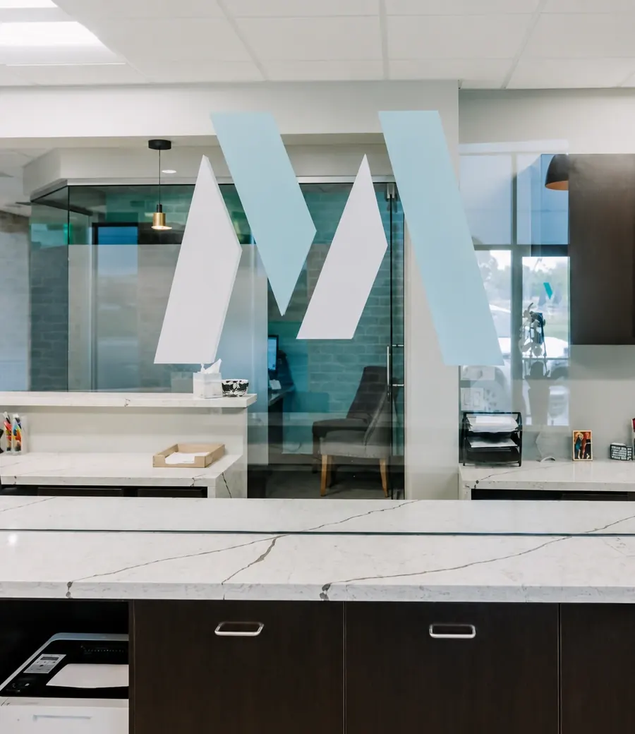 The front desk under the practice's large M mark, seen through glass.