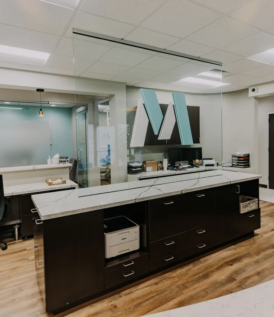 A reception area with a marble-topped front desk and the Montz & Maher M on the wall.