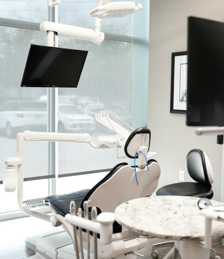A treatment room with a patient chair by the window and a ceiling-mounted screen.